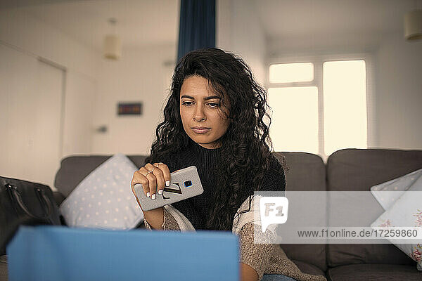 Frau arbeitet von zu Hause aus mit Smartphone und Laptop auf dem Sofa