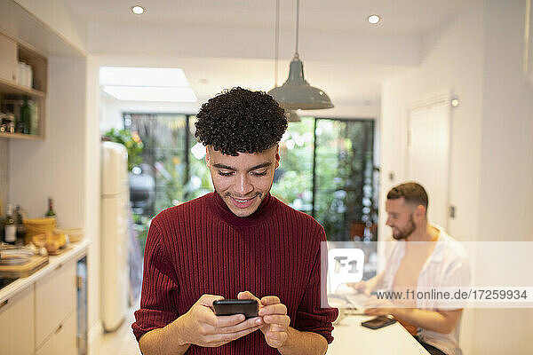 Junger Mann mit Smartphone in der Küche