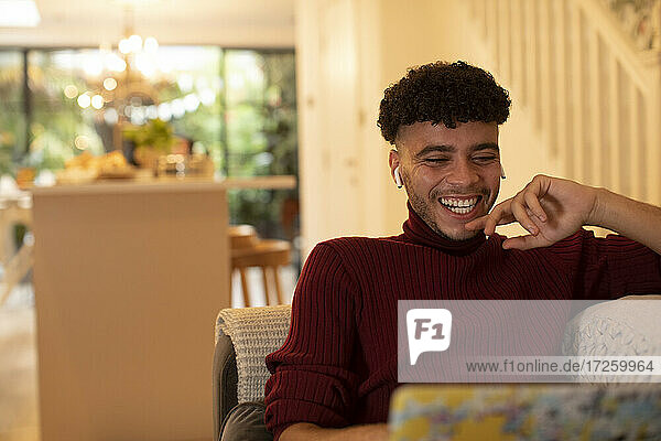 Glücklicher junger Mann mit Ohrstöpsel Kopfhörer beobachten Film auf Laptop