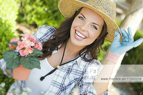 Attractive happy young adult woman wearing hat gardening outdoors