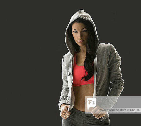 Studio portrait of woman in sports bra and hooded shirt
