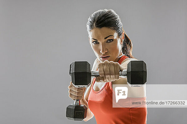 Studio-Porträt der sportlichen Frau in rotem ärmellosen Top  die mit Hanteln trainiert
