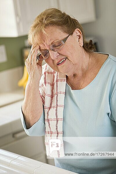 Grimassierende ältere Frau an der Küchenspüle mit Kopfschmerzen