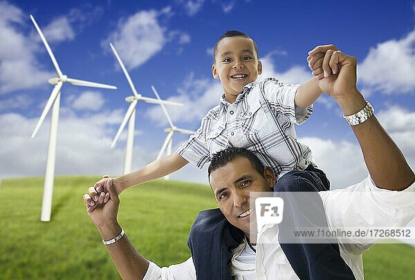 Happy hispanic father and son with wind turbine farm over blue sky