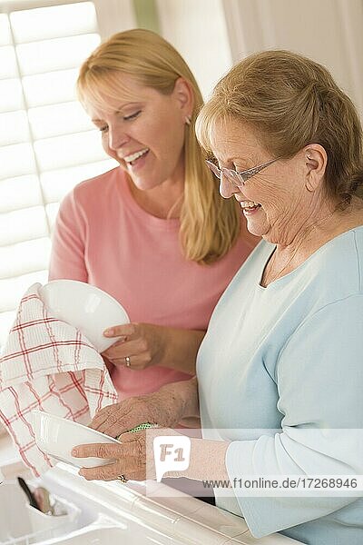 Lächelnde ältere Frau und junge Tochter im Gespräch am Waschbecken in der Küche
