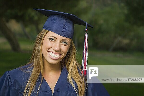 Smiling young woman wearing cap and gown outdoors