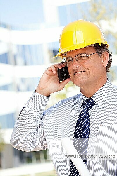 Gutaussehender Bauunternehmer mit Schutzhelm und Krawatte lächelt  während er in sein Handy spricht