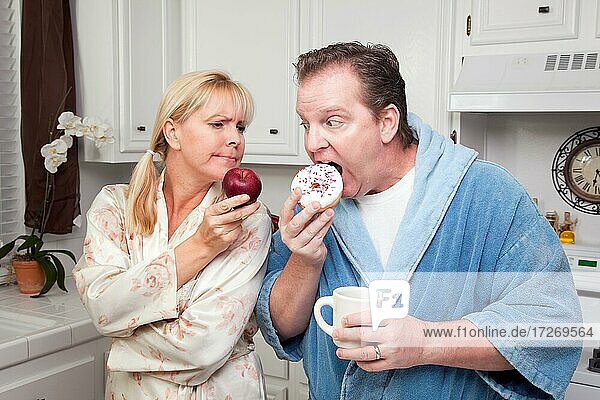 Couple in kitchen eating donut and coffee or healthy fruit