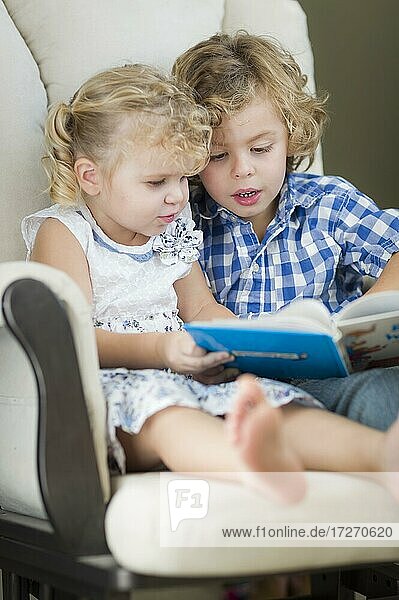 Cute young brother and sister reading a book together in a chair