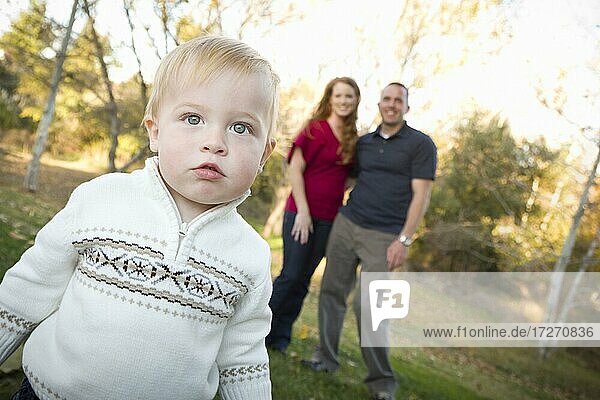 Cute young boy walking in the park as adoring parents look on from behind
