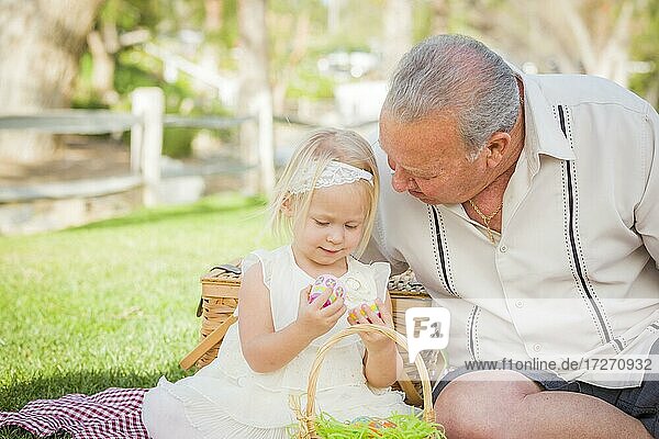 Loving grandfather and granddaughter enjoying easter eggs on a picnic blanket at park