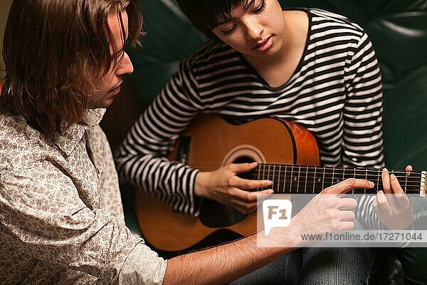 Junger männlicher Musiker bringt einer Schülerin das Gitarrenspiel bei