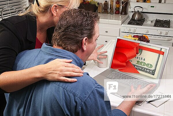 Couple in kitchen using laptop with stack of money wrapped in a red ribbon on the screen