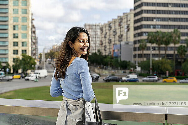 Lächelnde schöne Geschäftsfrau steht am Geländer  während die Stadt im Hintergrund