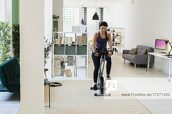 Young woman exercising while sitting on exercise bike at home