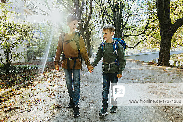 Junge hält die Hand seines jüngeren Bruders bei einem Spaziergang in einem öffentlichen Park an einem sonnigen Tag