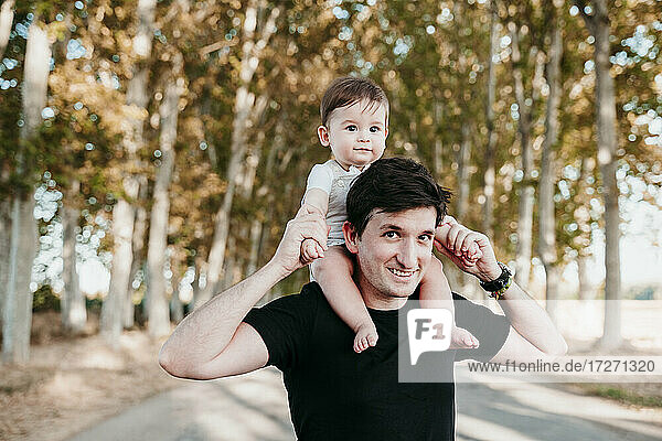 Father carrying baby boy on shoulder while standing outdoors