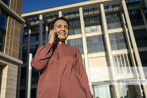 Geschäftsfrau  die mit ihrem Smartphone telefoniert  während sie an einem Gebäude steht
