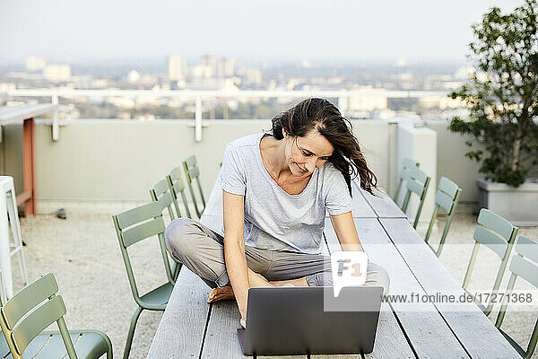 Reife Frau im Schneidersitz mit Laptop auf der Terrasse eines Gebäudes sitzend
