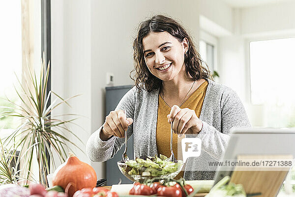 Lächelnde junge Frau  die zu Hause mit Hilfe eines digitalen Tablets Salat zubereitet