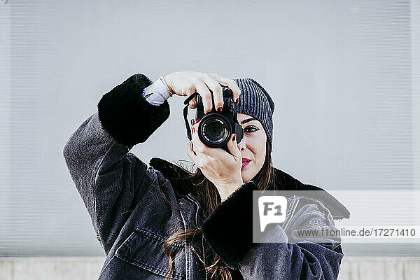 Selbstbewusste Frau  die durch die Kamera fotografiert  während sie an der Wand steht