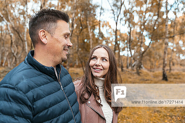 Smiling couple looking at each other while standing in park during autumn