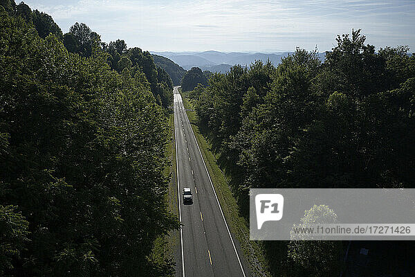 Luftaufnahme eines einsamen Autos auf der U.S. Route 58  die sich über einen grünen Bergwald erstreckt