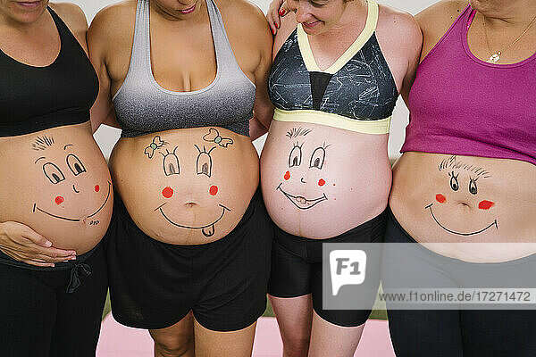 Midsection von schwangeren Frauen mit Gesicht Zeichnung auf Bauch stehend im Yoga-Studio