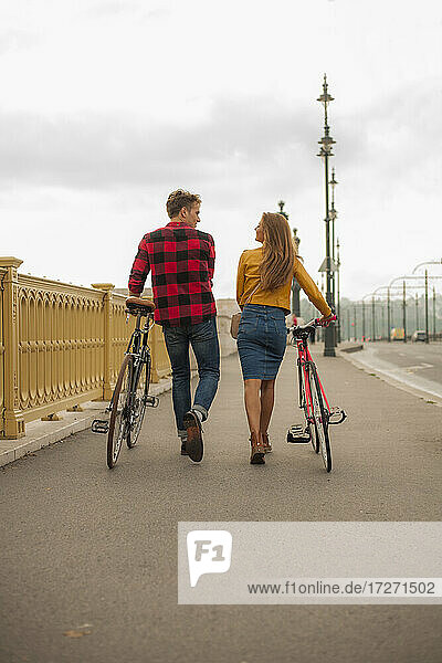 Lächelndes heterosexuelles Paar mit Fahrrad auf dem Gehweg in der Stadt