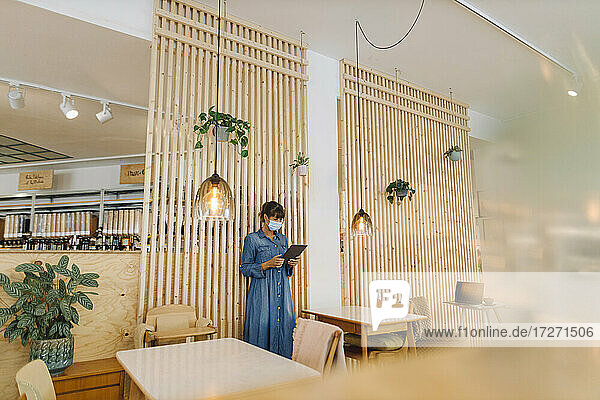 Unternehmerin bei der Nutzung eines digitalen Tablets an einer Holzwand in einem Café während der COVID-19