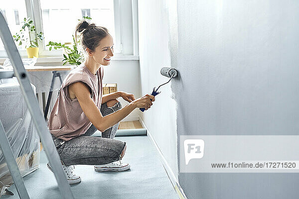 Junge Frau  die zu Hause hockend eine Wand mit einer Farbrolle streicht