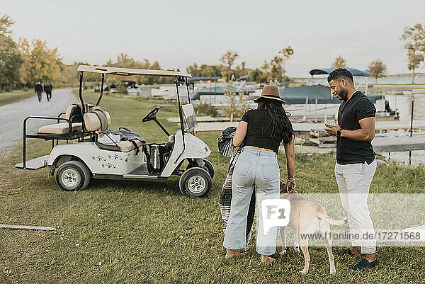 Ehepaar mit Hund steht neben Golfwagen im Freien