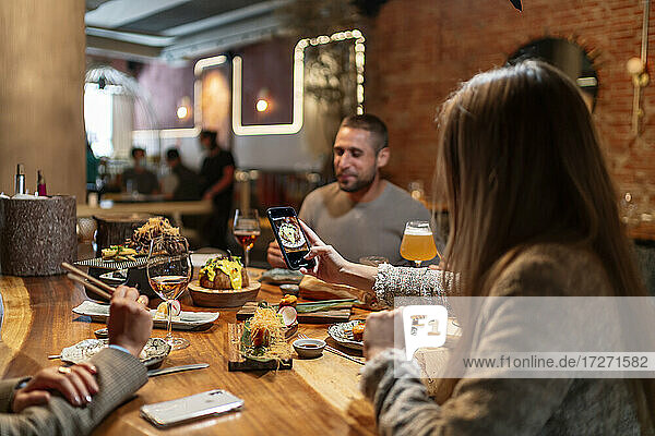 Junge Frau  die mit ihrem Handy ein Foto vom Essen macht  während sie mit Freunden im Restaurant sitzt