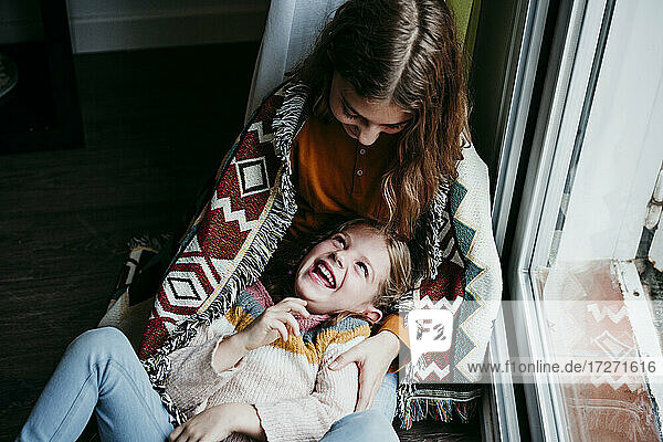 Verspieltes Mädchen  das lachend auf dem Schoß seiner Schwester zu Hause liegt