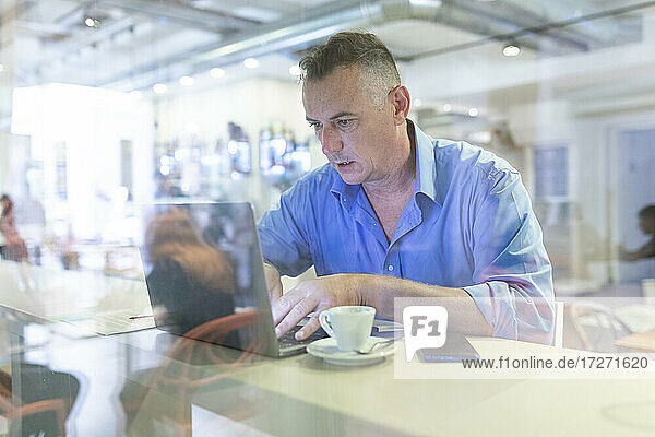 Männlicher Unternehmer  der einen Laptop benutzt  während er mit einem Kaffee im Café sitzt