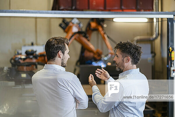 Businessman discussing while standing against robotic arm machine at modern factory