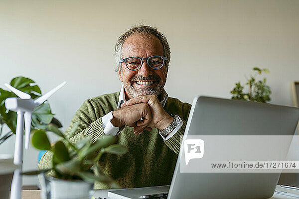 Smiling man wearing eyeglasses using laptop while sitting by table at home