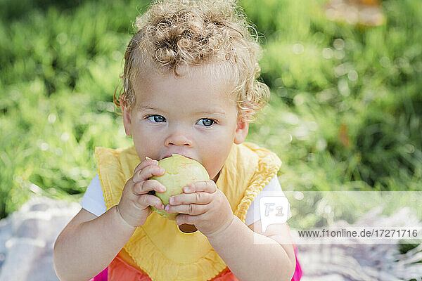 Süßes Baby Mädchen essen Obst,  während auf Gras im Park sitzen