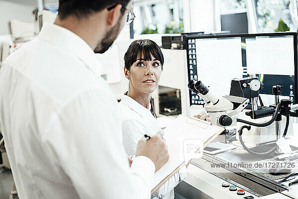 Geschäftsfrau schaut auf Geschäftsmann mit Klemmbrett im Labor stehend