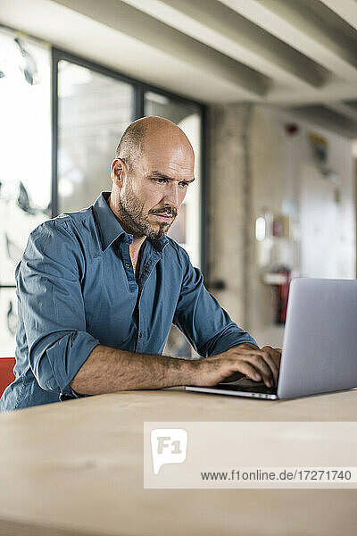 Geschäftsmann arbeitet am Laptop  während er am Tisch im Büro sitzt