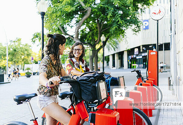 Lesbian couple smiling at each other while standing at bicycle parking station