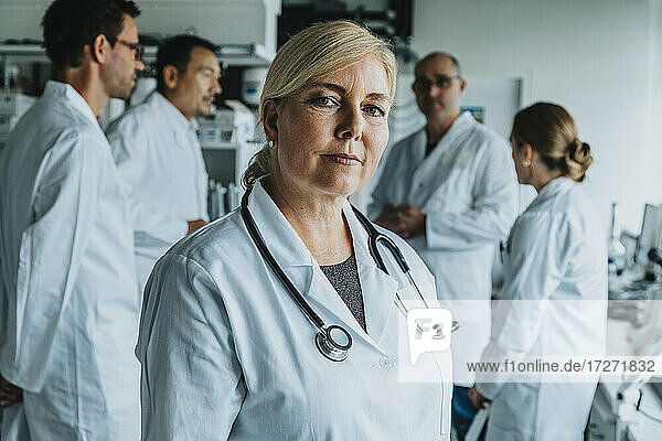 Lächelnde Wissenschaftlerin  die wegschaut  während sie mit einem Mitarbeiter im Hintergrund im Labor steht