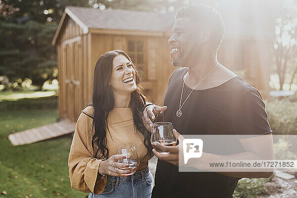 Glückliches Paar mit Weinglas  das lächelnd im Hinterhof steht