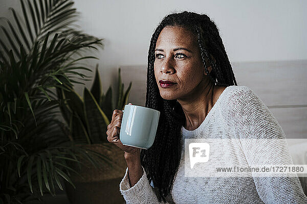 Reife Frau trinkt Kaffee  während sie zu Hause sitzt