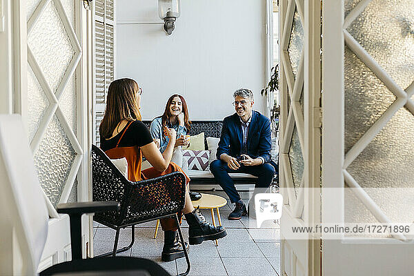 Smiling female entrepreneur discussing with coworkers while having coffee on sofa in balcony