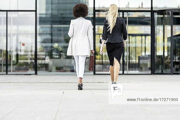 Businesswomen walking on footpath against building