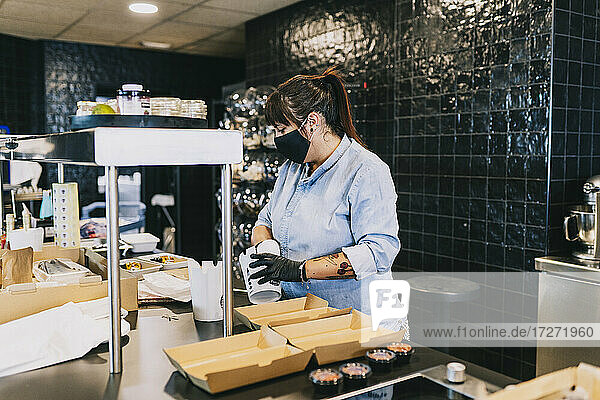 Mid adult female chef preparing take out food containers at counter in restaurant during COVID-19
