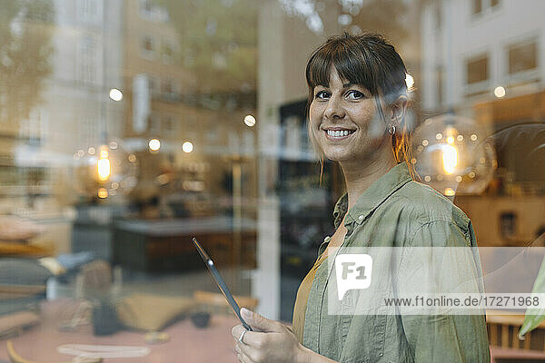 Female entrepreneur using digital table looking through window while standing in coffee shop