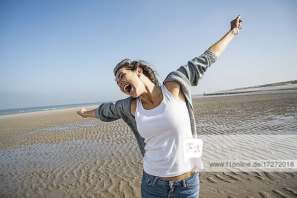 Carefree young woman with arms outstretched at beach against clear sky