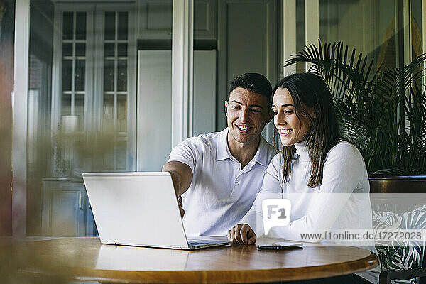 Lächelnder Mann und lächelnde Frau benutzen einen Laptop  während sie zu Hause sitzen